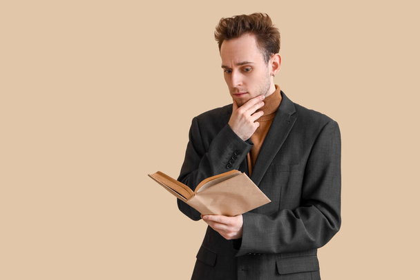 Nachdenklicher junger Mann liest Buch auf beigem Hintergrund - Foto, Bild