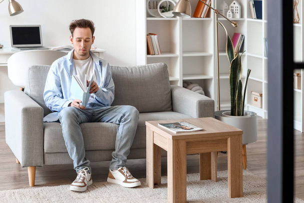 Young man reading book on sofa at home - Фото, зображення