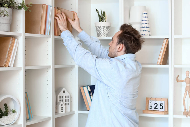 Young man taking book from shelf at home - Foto, Imagem