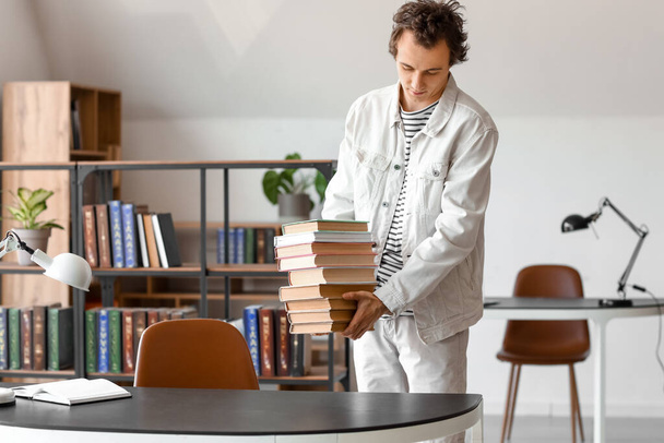 Молодой человек со стопкой книг в библиотеке - Фото, изображение