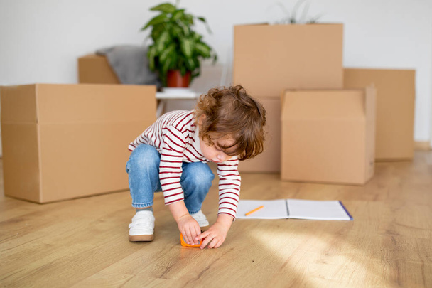 Cute Little Boy Playing With Tape Ruler At Home During Moving Day, Playful Toddler Child Measuring Floor While Spending Time In Living Room Among Cardboard Boxes With Belongings, Copy Space - Photo, Image