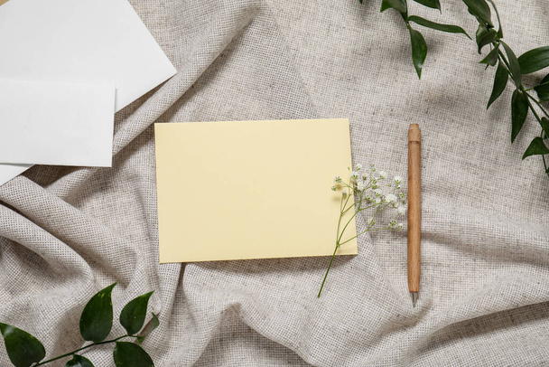 Пустой пригласительный билет, ручка, цветы гипсофилы и эвкалиптовые ветви на серой скомканной скатерти - Фото, изображение