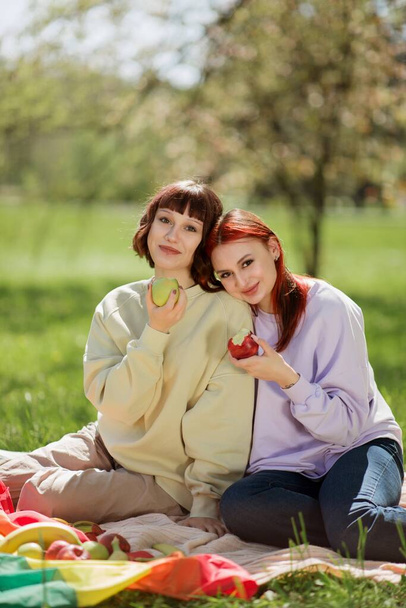 Lesbian ladies have a picnic in the middle of the park they eating some fruits and feeling very happy and relaxed. - Foto, Imagem