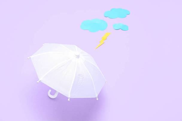Σύνθεση με ομπρέλα, χάρτινα σύννεφα και αστραπή σε λιλά φόντο - Φωτογραφία, εικόνα