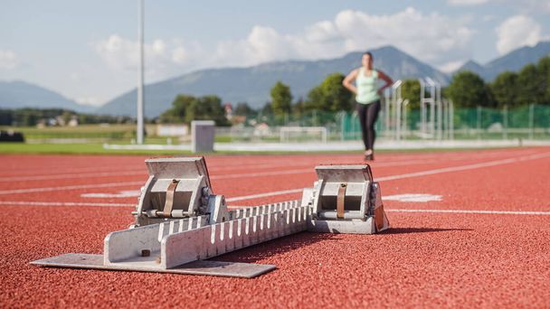 Starting block device placed on an athletic track, approached by a female silhouette from the distance, close up shot. - 写真・画像
