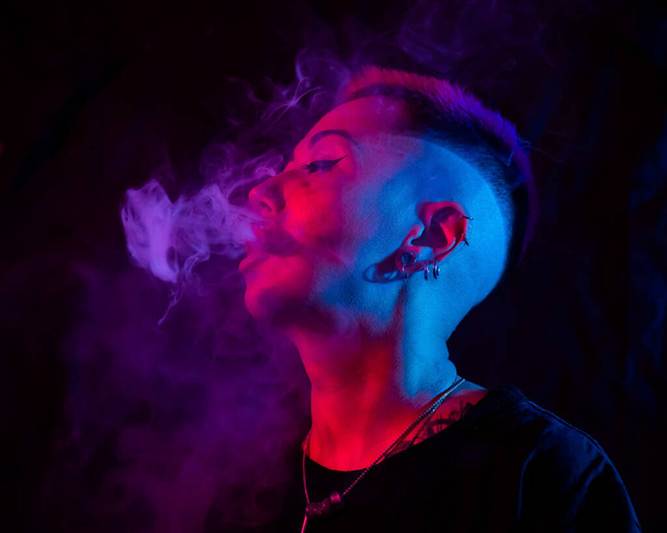 Profile Asian woman with short haircut smoking in neon light - Фото, изображение