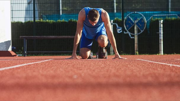 Front view of a Caucasian male sprinter in a race starting position, hands on the line and legs on starting block - 写真・画像