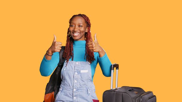 アフリカ系アメリカ人女性はカメラに親指を立て、合意と承認を表明した。若い観光客のような表示と成功のシンボルは、休暇の旅の目的地で肯定的な女の子。手持ち撮影. - 写真・画像