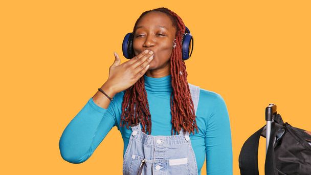 Afro-Amerikaans meisje geeft luchtkussen en luistert naar muziek op de headset, flirt en romantisch in de studio. Jonge glimlachende toeristische dansen en het gevoel vrolijk, schattig symbool. Handschot. - Foto, afbeelding