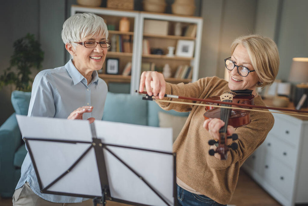 Dwie dorosłe kobiety nauczyciel dać prywatne lekcje skrzypiec do jej ucznia lub przyjaciela w domu pomóc jej nauczyć się grać w pokoju hobby i rekreacji aktywnego seniora koncepcji przestrzeni kopii - Zdjęcie, obraz