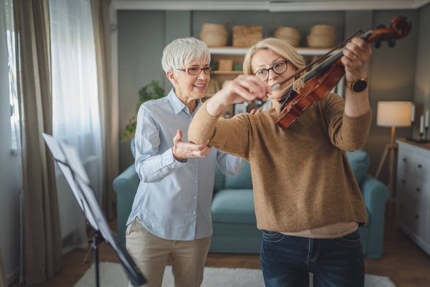 Zwei reife Lehrerinnen geben ihrem Schüler oder Freund zu Hause privaten Geigenunterricht und helfen ihr, das Spielen im Raum zu erlernen. - Foto, Bild