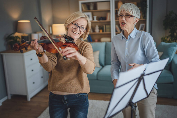 Δύο γυναίκες ώριμη δασκάλα δώσει ιδιωτικό μάθημα βιολιού στο μαθητή ή το φίλο της στο σπίτι να τη βοηθήσει να μάθουν να παίζουν στο χώρο χόμπι και αναψυχής ενεργό ανώτερος έννοια αντίγραφο χώρο - Φωτογραφία, εικόνα