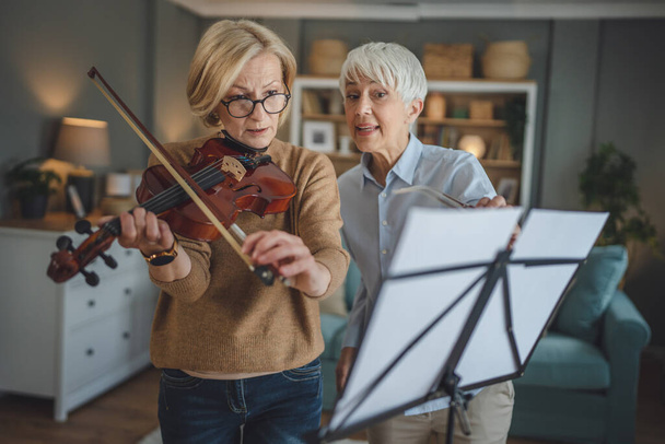 Dwie dorosłe kobiety nauczyciel dać prywatne lekcje skrzypiec do jej ucznia lub przyjaciela w domu pomóc jej nauczyć się grać w pokoju hobby i rekreacji aktywnego seniora koncepcji przestrzeni kopii - Zdjęcie, obraz