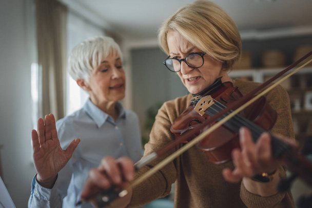 Duas mulheres maduras professora dar aula de violino privado para seu aluno ou amigo em casa ajudá-la a aprender a jogar no quarto hobby e lazer espaço de cópia conceito sênior ativo - Foto, Imagem