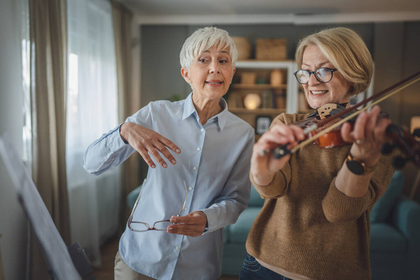 Deux femmes enseignantes matures donnent une leçon privée de violon à son élève ou à son ami à la maison l'aident à apprendre à jouer dans la pièce passe-temps et loisirs active senior concept copy space - Photo, image