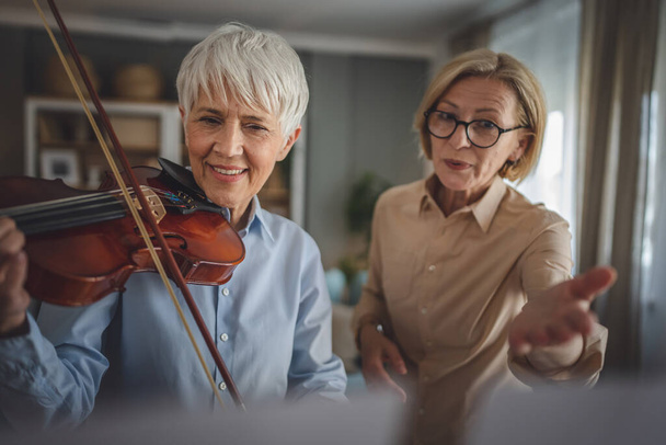 Две зрелые женщины учитель дать частные уроки скрипки для своего ученика или друга на дому помочь ей научиться играть в комнате хобби и досуга активный старший концепт копирования пространство - Фото, изображение