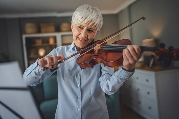 Зрелая старшая белая женщина учится играть на скрипке дома - Фото, изображение