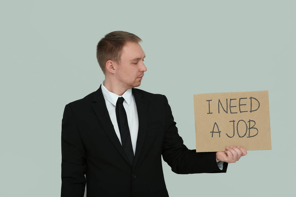 Unemployed man holding sign with phrase I Need A Job on light grey background - Foto, Imagen