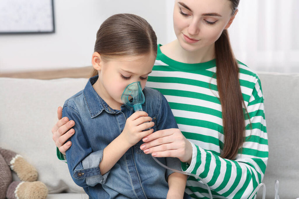 Mother helping her sick daughter with nebulizer inhalation at home - Фото, зображення