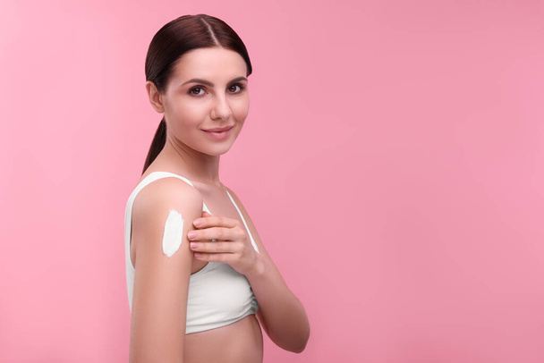 Beautiful woman with smear of body cream on her shoulder against pink background. Space for text - Foto, Imagem