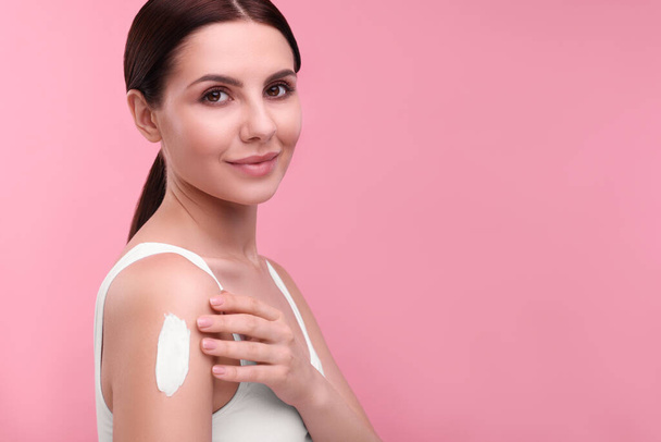 Beautiful woman with smear of body cream on her shoulder against pink background. Space for text - Fotó, kép