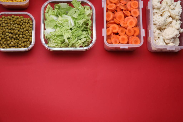 Plastic and glass containers with different fresh products on red background, flat lay. Space for text - Fotografie, Obrázek