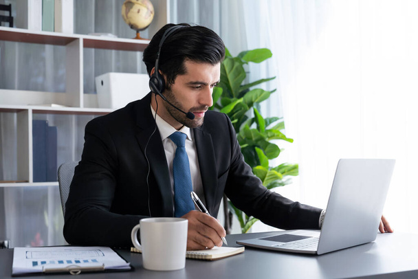 Male call center operator or telesales representative siting at his office desk wearing headset and engaged in conversation with client providing customer service support or making a sale. fervent - Zdjęcie, obraz