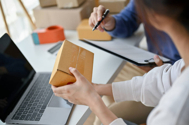 Close-up image of a female online seller checking orders and examining a shipping box before shipment. Small business, E-commerce, online selling, Website admin - Photo, Image