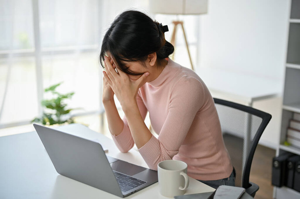 Αγχωμένη και απογοητευμένη Ασιάτισσα επιχειρηματίας που καλύπτει το πρόσωπό της και κλαίει στο γραφείο της ενώ έχει άγχος από τη δουλειά της. - Φωτογραφία, εικόνα