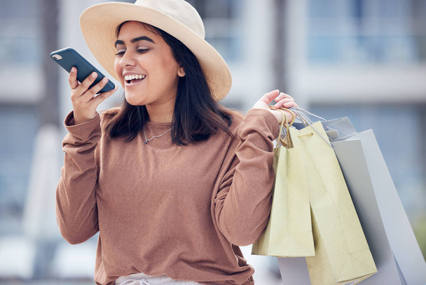 Shopping, voice note and happy Indian woman in city for communication, conversation and chat. Retail, fashion and female person talking on smartphone with bags for sale, bargain and discount purchase. - Photo, Image