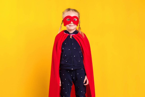 Niña superhéroe con un impermeable rojo y una máscara sobre un fondo amarillo. Estudio fotografía - Foto, Imagen