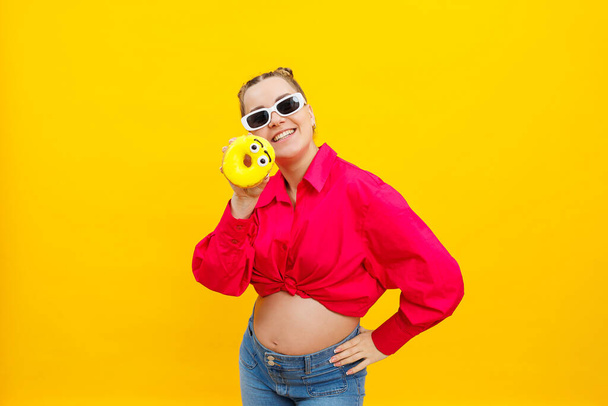 Positieve zwangere vrouw die donuts eet met een roze shirt op een gele achtergrond. Geluk van de zwangerschap tijdens de zwangerschap. Hoge kwaliteit foto. Schadelijk voedsel tijdens de zwangerschap - Foto, afbeelding