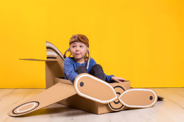 Little dreamer girl playing with a cardboard airplane. Childhood. Fantasy, imagination. Studio photography on a yellow background. Imagination or exploration concept - Foto, afbeelding