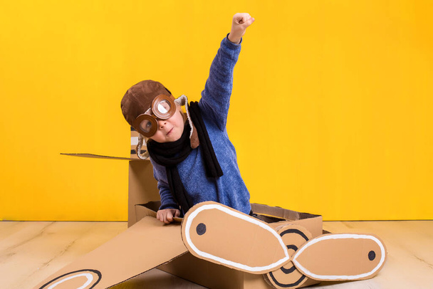 Kleines Träumermädchen beim Spielen mit einem Pappflugzeug. Kindheit. Fantasie, Fantasie. Studioaufnahmen auf gelbem Hintergrund. Fantasie oder Explorationskonzept - Foto, Bild
