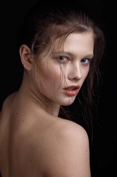 Beauty shooting at the studio, black background. Model with a clear shiny face, natural make up, wet hair. Blue eyes and shiny lips. - Photo, image