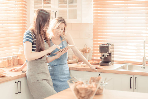 Beautiful lesbian couple cooking healthy food, looking on digital tablet at modern kitchen interior. Homosexual relations and healthy eating concept. LGBT,LGBTQ home online kitchen. warm tone. - Foto, immagini