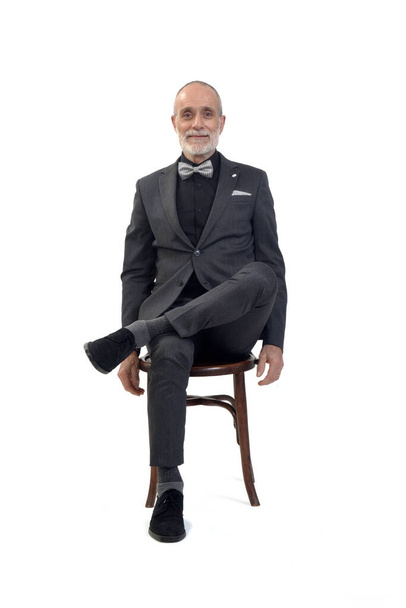 front view of a man sitting  on chair with suit and bow tie and cross legged on white background - Foto, Bild