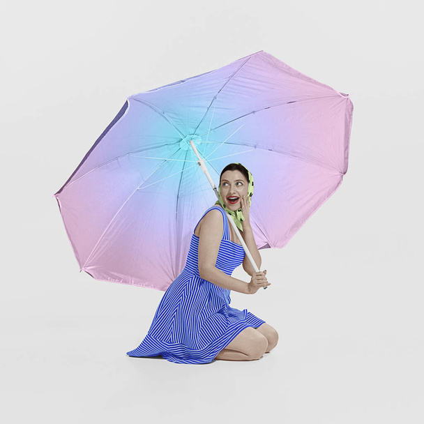 Happy excited young beautiful girl sitting under big sun beach umbrella. Retro vintage photo style, 70s, 80s fashion, beauty and ad concept. Rainbow palette. Copy space for ad. Model looks surprised - 写真・画像