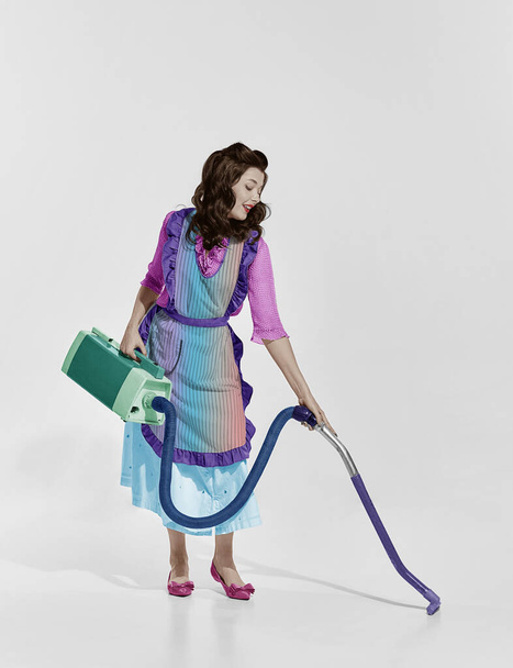 Charming housewife. Portrait of elegant retro woman cleaning house with vacuum cleaner. Rainbow style palette. Concept of beauty, retro, fashion, elegance, 60s, 70s, house cleaning. Copy space for ad - Φωτογραφία, εικόνα