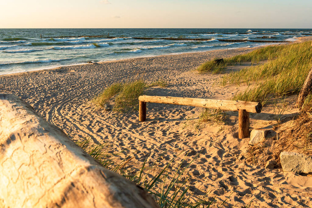 Belépés egy gyönyörű strandra a Balti-tengeren naplementekor. Fa korlát, dűnék, fű és fenyőfák. Darlowo, Lengyelország - Fotó, kép