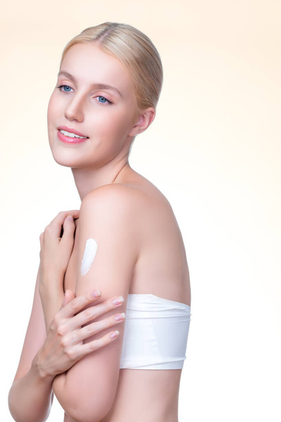 Personable beautiful woman putting skincare moisturizer cream on her arm looking in camera in isolated background as concept for beauty care treatment. Female model applying lotion on her body. - Foto, immagini