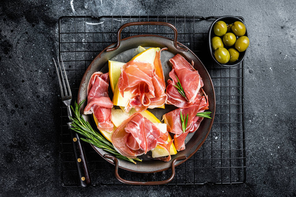 Italian prosciutto parma with melon and fresh rosemary. Black background. Top view. - Foto, Imagem