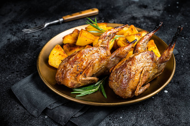 Delicious roasted quails with herbs in a plate with fried potato. Black background. Top view. - Foto, imagen