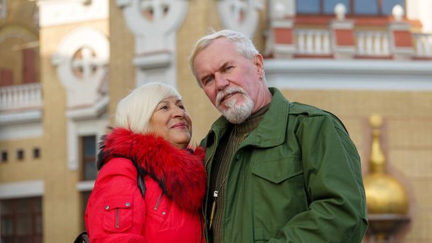 Portrait of an elderly gray-haired couple, a man in militarized khaki clothes, a woman in an orange jacket, in autumn in the city - Foto, imagen