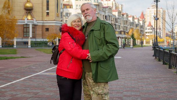 Retrato de una pareja de ancianos de pelo gris, un hombre con ropa militarizada de color caqui, una mujer con una chaqueta naranja, en otoño en la ciudad - Foto, imagen