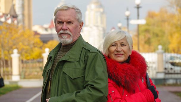 高齢者の白髪のカップルの肖像、軍事化されたカーキの服の男、オレンジのジャケットの女性、街の秋 - 写真・画像