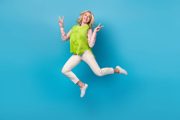 Full body photo of pretty overjoyed lady jumping demonstrate v-sign isolated on blue color background. - Foto, immagini