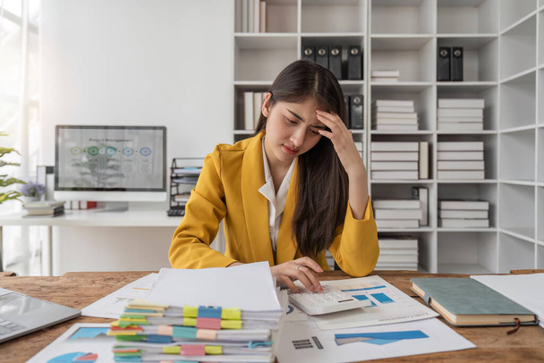 Las mujeres de negocios están estresadas mientras trabajan en el ordenador portátil y pila de documentos, empresaria cansada con dolor de cabeza en la oficina, sintiéndose mal en el trabajo. - Foto, imagen