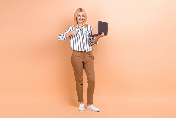 Full length photo of adorable confident lady wear striped shirt working gadget thumb empty space isolated beige color background. - Fotoğraf, Görsel