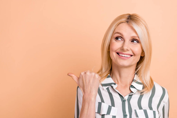Photo of pretty positive person toothy smile look direct finger empty space isolated on beige color background. - 写真・画像